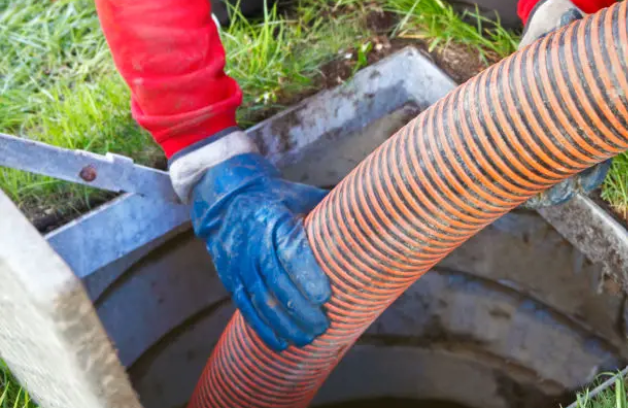 Worker guiding an orange vacuum hose while cleaning a cesspit